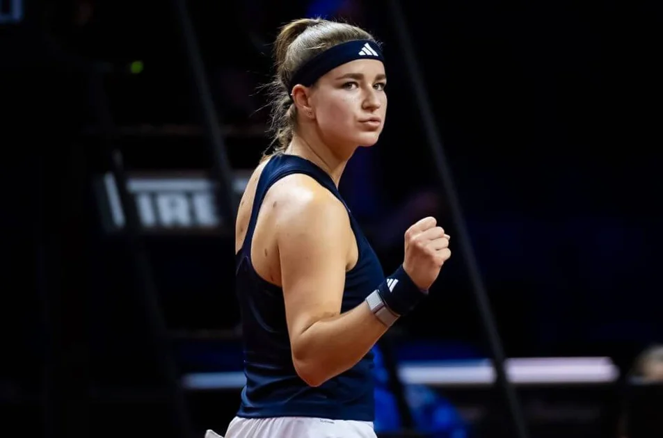 Karolína Muchová pumps her right fist as she turns to ther right wearing a navy tennis outfit and headband.