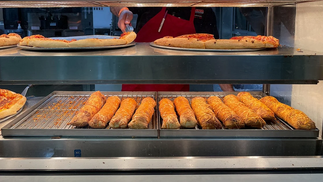 Close up view of Costco food court with an employee getting the pepperoni pizza from the tray with chicken bakes below
