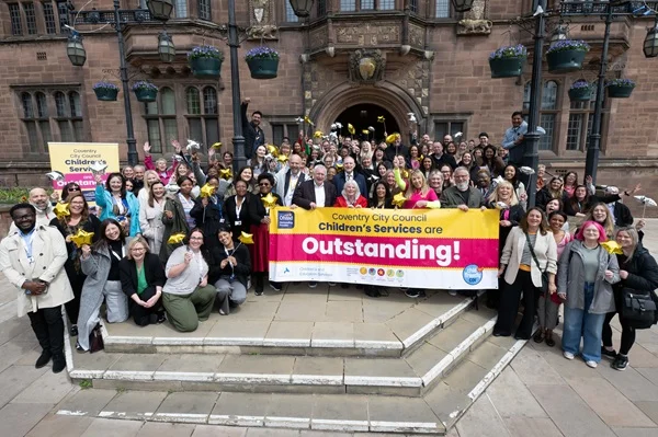 Coventry City Children Service's staff outside the Council House holding up banner that says 'Outstanding'.