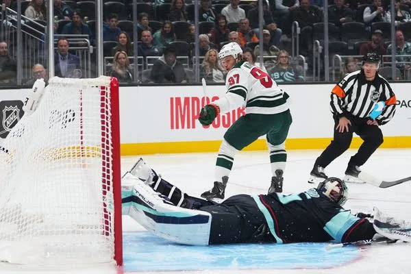A hockey player looks behind him after scoring a goal as the opposing goalie lies on his stomach.